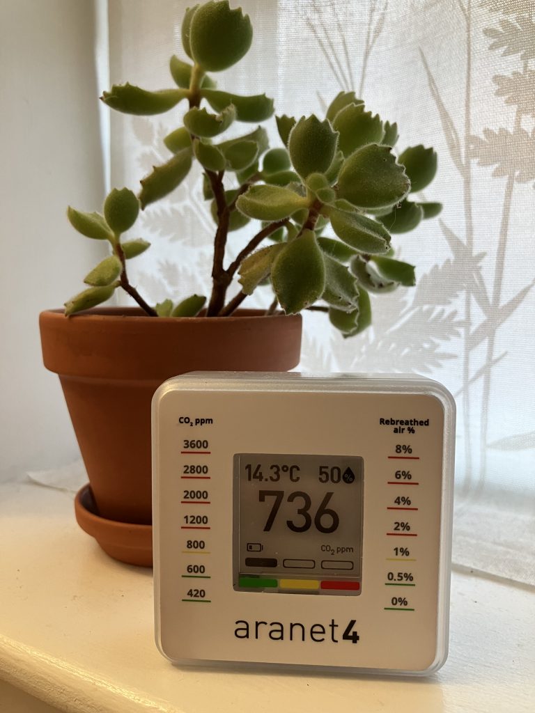 An aranet4 air quality monitor with a potted plant.