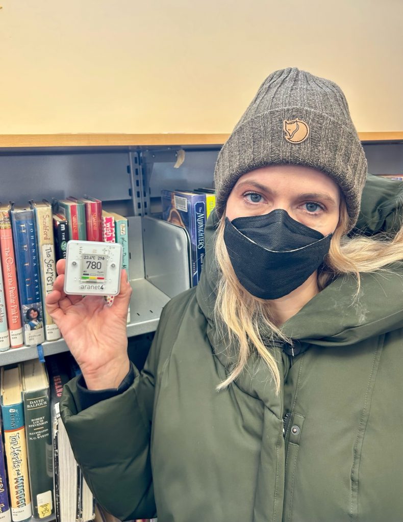 Woman holding at Aranet CO2 monitor inside a library.